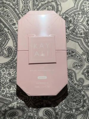 Kayali Yum Boujee Marshmallow 100ml - Kayali Yum Boujee Marshmallow 51 Intense Eau de Parfum i en snygg ljusrosa, åttakantig kartong. Flaskan rymmer 100 ml och doften är känd för sina söta och gourmandiga toner. Perfekt för dig som gillar unika och lyxiga parfymer.