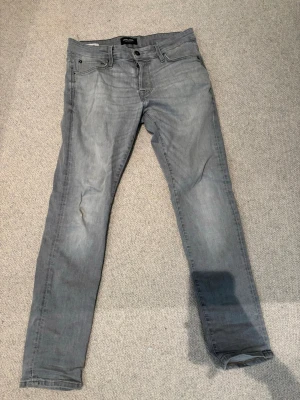Grå slim fit jeans från Jack & Jones - Snygga grå slim fit jeans från Jack & Jones med klassisk femficksdesign och dragkedjegylf. Jeansen har en lätt tvättad look och raka ben, perfekta för en avslappnad stil.