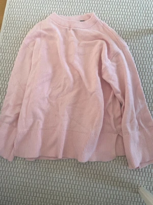 Ljusrosa oversized stickad tröja - Mysig ljusrosa stickad tröja med oversized passform och breda ribbade muddar vid ärmslut och nederkant. Tröjan har rund halsringning och är tillverkad i mjukt material som känns skönt mot huden. Perfekt för lager på lager och en avslappnad look.