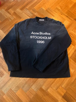 Svart longsleeve Acne Studios - Cool svart longsleeve  från Acne Studios med vit text 'Acne Studios STOCKHOLM 1996' på bröstet. Tröjan har rund halsringning och långa ärmar. Perfekt för dig som gillar minimalistisk och stilren design. Skriv vid funderingar!  