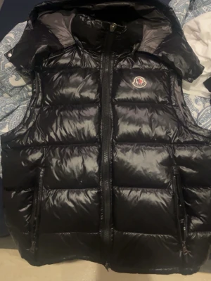 Moncler väst - Snygg svart dunväst från Moncler med glansigt material, två dragkedjefickor och Moncler-logga på bröstet. Västen har hög krage och quiltad design som ger en modern look. Perfekt för lager-på-lager och streetstyle. Den är S men passar M också. Priset går att diskuteras.