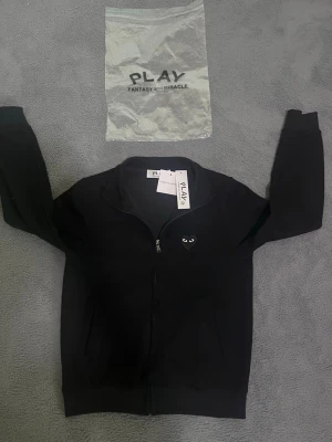 CDG ZIPPER HOODIE - ✅ Helt svart CDG zipper med lappen kvar   ✅ Helt ny & oanvänd   ✅ Stilren och clean design   ✅ Passar till allt   ✅ Perfekt fit & hög kvalitet   ✅ Storlek XS   ✅ Påsen i bilden inkluderars när köp genomförs 
