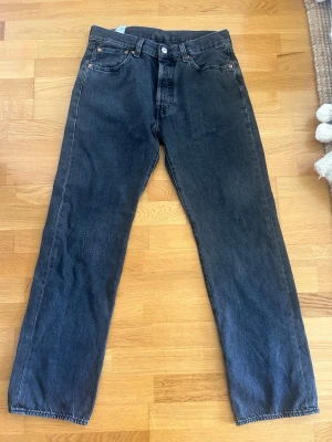 Svarta Levi's 501 jeans straight fit - Klassiska svarta Levi's 501 jeans med rak passform och fem fickor. Jeansen har knappgylf och är tillverkade i kraftig denim. Perfekta för en avslappnad och tidlös stil.