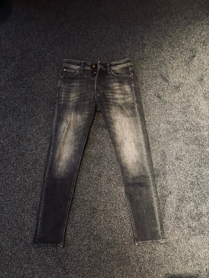 Svarta slim fit jeans med slitningar - Snygga svarta slim fit jeans med slitna detaljer och tvättad look. Klassisk femficksmodell med dragkedja och knapp i midjan. Jeansen har en modern passform och är perfekta för en trendig streetstil.