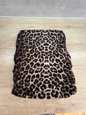 Leopardmönstrad bandeau tubtopp - Snygg bandeau tubtopp med leopardmönster i bruna och svarta toner. Toppen är ärmlös och har en tight passform, perfekt att styla till jeans eller kjol. Materialet känns mjukt och stretchigt, vilket gör den bekväm att bära hela dagen.