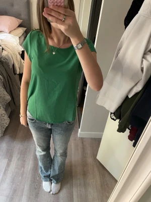 Grön topp från ONLY - Snygg grön topp från ONLY med rund halsringning och korta ärmar. Tunn och lätt i materialet, perfekt för varmare dagar. Enkel och stilren design som är lätt att matcha med jeans eller kjol.