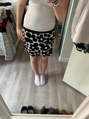Blommig svartvit kjol  - Snygg kort kjol från H&M Divided med svartvitt blommönster. Kjolen har en rak passform och är tillverkad i ett mjukt, stickat material som känns bekvämt. Perfekt för dig som vill sticka ut med en cool och trendig look.