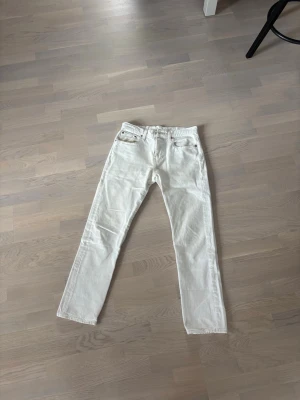Levis Vita raka jeans med kopparknappar - Snygga vita jeans med rak passform och klassiska fem fickor. Jeansen har kopparfärgade knappar och detaljer, samt bälteshällor. Perfekta för en fräsch och stilren look. W30 L30 TVÄTTAS INNAN KÖP! 