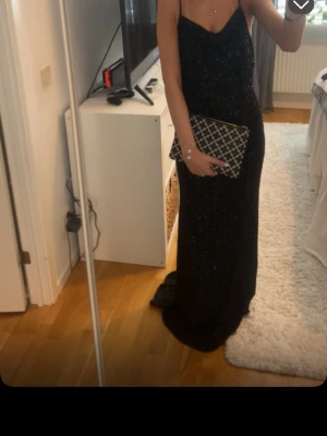 Svart glittrig långklänning balklänning  - Säljer en svart långklänning med tunna axelband och öppen rygg. Klänningen har ett glittrigt tyg som fångar ljuset och ger en lyxig känsla. Perfekt för dig som vill sticka ut på bal eller fest. Snygg och elegant passform med släp.lite slitningar där nere men inget man ser eller tänker på,jag tror den är från dressroom❤️