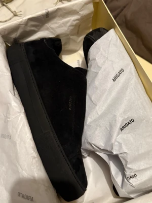 Svarta sneakers från Axel Arigato - I princip helt nya och stil svarta sneakers från Axel Arigato i mocka med diskret logga i guld på sidan. Skorna har en chunky svart sula och minimalistisk design som passar till det mesta. Perfekta för dig som gillar en clean och modern look.