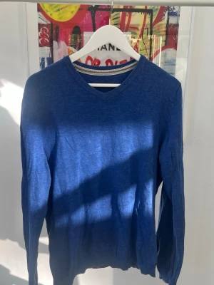 Blå V-ringad tröja Esprit - Snygg blå V-ringad tröja från Esprit med långa ärmar. Tröjan har en enkel och stilren design med ribbade muddar vid hals, ärmslut och nederkant. Perfekt att matcha med jeans eller chinos för en clean look.