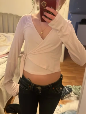 Ljusrosa omlottopp från Gina Tricot - Supersöt ljusrosa omlottopp från Gina Tricot med långa ärmar och knyt i sidan. Toppen är croppad och har en mjuk, stretchig känsla som passar perfekt till jeans eller kjol. Enkel men ändå stylish design som är lätt att matcha.