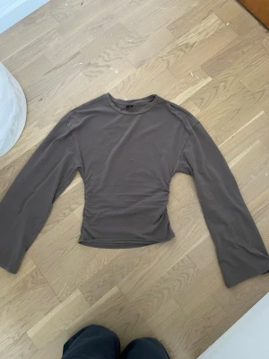 Brun långärmad topp från Gina Tricot - Säljer en brun långärmad topp från Gina Tricot. Toppen har en enkel och stilren design med rund halsringning och är tillverkad i mjuk bomull. Perfekt att matcha med jeans eller kjol för en snygg look.