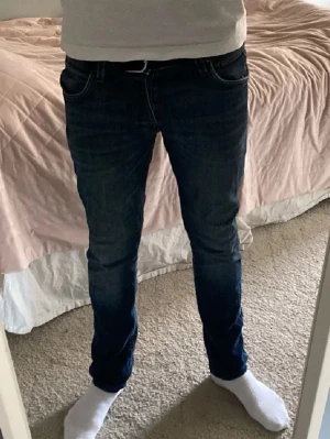 Mörkblå slim fit jeans - Snygga mörkblå slim fit jeans med klassisk femficksdesign och normal midja. Jeansen har en smal passform längs benen och är tillverkade i ett stretchigt denimtyg som ger en bekväm känsla. Perfekta för en trendig och avslappnad look.