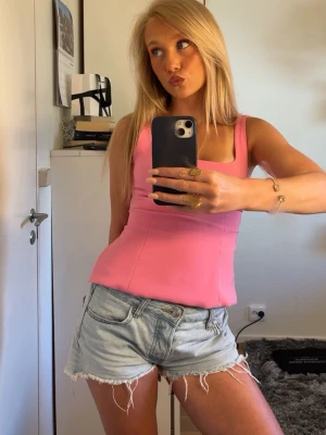 Rosa linnetopp med rosett Zara - Superfin rosa linnetopp med breda axelband och stor rosett framtill. Toppen har figurnära passform och är perfekt för en färgglad look. Materialet känns mjukt och lätt, perfekt för varma dagar.