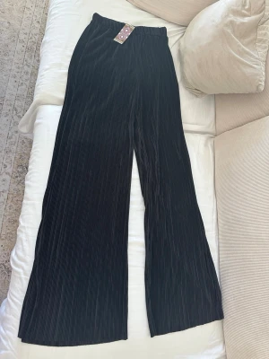 Svarta plisserade vida leggings - Snygga svarta leggings med plisserat tyg och vida ben. De har resår i midjan för en bekväm passform och är perfekta för en trendig och avslappnad stil. Materialet är mjukt och följsamt, vilket gör dem riktigt sköna att bära.
