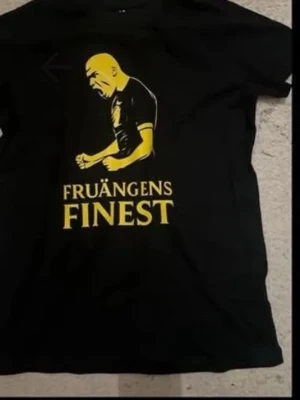 Svart t-shirt Fruängens Finest - Cool svart t-shirt med gult tryck av en person och texten 'Fruängens Finest' på framsidan. Klassisk passform och rund hals. Perfekt för dig som vill sticka ut med en unik och lokal stil.