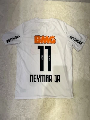 Vit Santos Neymar Jr matchtröja - Säljer en vit Santos FC matchtröja från Nike med Neymar Jr och nummer 11 på ryggen. Tröjan har tryckta sponsorer som BMG och Netshoes, samt klubbmärke på bröstet. Tillverkad i Dri-FIT material som andas, perfekt för fotboll eller träning.