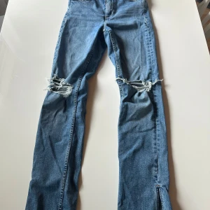 Blå slitna jeans från Zara - Säljer ett par blåa högmidjade jeans från Zara med snygga slitningar över knäna och raka ben med slits längst ner. Jeansen är väldigt bekväma att ha på sig. Använda ett fåtal gånger. Är 162 och dem är bra i längden. 