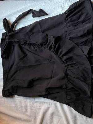 Svart omlottkjol med volang från ONLY - Snygg svart omlottkjol från ONLY i storlek XS. Kjolen har volangdetaljer längs kanten och knyts i midjan för en trendig look. Perfekt för dig som gillar stilrena och feminina plagg.