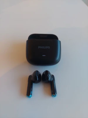 Svarta trådlösa in-ear hörlurar Philips - Snygga svarta trådlösa in-ear hörlurar från Philips med laddningsetui. Hörlurarna har en stilren och modern design i blank plast och laddas smidigt i det medföljande etuiet. Perfekta för musik, poddar och samtal på språng.