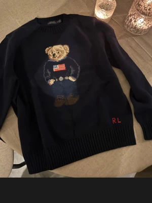 Mörkblå stickad tröja med björn - Mörkblå stickad tröja från Ralph Lauren med ett björn i mitten passar alla kläd typer och alla personer 
