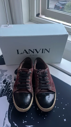 Lanvin sneakers i vinröd mocka - Snygga sneakers från Lanvin i vinröd mocka med svarta lackade tår och svarta skosnören. Skorna har en klassisk låg modell och vit sula som ger en stilren kontrast. Perfekta för dig som vill ha en unik och trendig look.