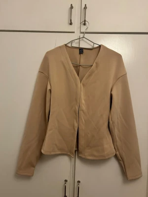 Beige cardigan från SHEIN - Stilren beige cardigan från SHEIN i storlek S. Koftan har en enkel design med V-ringning och långa ärmar. Tillverkad i ett mjukt och stretchigt material som känns skönt mot huden. Perfekt att slänga över en topp för en clean look.