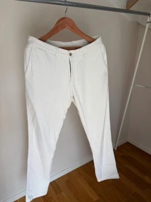Vita chinos med rak passform - Snygga vita chinos med smal passform och klassisk design. Byxorna har bälteshällor, två sidofickor fram och två bakfickor med knapp. Tillverkade i ett lätt bomullstyg som passar perfekt till en avslappnad men stilren look.