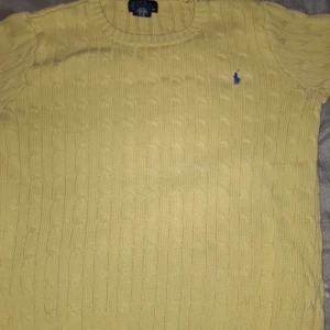Gul stickad tröja från Ralph Lauren - Säljer en gul stickad tröja från Ralph Lauren med kabelstickat mönster. Tröjan har korta ärmar och en liten blå logga på bröstet. Perfekt för en stilren look!