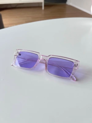 Solglasögon med lila glas, Gina Tricot - Ett par solglasögon med lila glas och transparenta/rosa bågar från Gina Tricot. Använda en gång, nyskick.  Ingår ett fodral + putsduk.