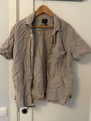 Beige skjorta från H&M - Kortärmad beige skjorta från H&M. Perfekt för varma dagar och enkel att styla till olika outfits.