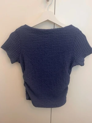 Mörkblå ribbad topp - En mörkblå ribbad topp med korta ärmar och rund hals. Tyget har en stretchig struktur som ger en skön och avslappnad passform. Perfekt att matcha med jeans  för en enkel och snygg look.