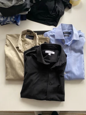 3-pack skjortor Riley & MQ, S - Säljer tre stilrena skjortor i storlek S: en ljusblå Riley slim fit, en beige från MQ och en svart från SMRG. Alla har klassisk krage och knäppning framtill. Perfekta för dig som vill ha enkla och snygga skjortor i garderoben.