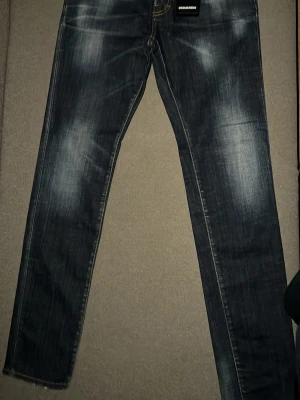 Mörkblå Dsquared2 jeans herr - Snygga mörkblå jeans från Dsquared2 med slitna detaljer och kontrastsömmar. Klassisk femficksmodell med raka ben och tydlig logotyp på fickan. Jeansen har en cool tvättad look och är tillverkade i bomull för skön känsla. Helt nya, aldrig använda nypris på de låg på 5799kr men jag köpte de med 40% rabbat. Säljer för att de inte är min stil och för att de är aldrig använda. 