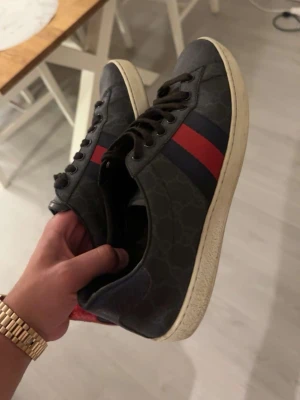 Gucci ace skor  - Snygga svarta sneakers med röd och mörkblå rand på sidan samt vit sula. Skorna har lågt skaft och klassisk snörning. Materialet ser ut att vara läder eller mocka. Perfekta för en stilren och sportig look. Passar riktigt bra 43 också top skick 10/10