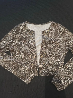 Leopardmönstrad croppad kofta - Snygg croppad kofta med leopardmönster i brunt, beige och svart. Långärmad modell med knäppning framtill. Tunn och stretchig kvalitet som passar perfekt till lager på lager eller som statement-plagg.