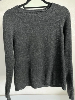 Mörkgrå stickad tröja Vero Moda - Mysig mörkgrå/svart stickad tröja från Vero Moda med rund halsringning och långa ärmar. Tröjan har ribbade muddar vid hals, ärmslut och nederkant. Perfekt för kyliga dagar och enkel att matcha till olika outfits. Tröjan är ganska använd men inga skador syns❤️ (Nypris 300kr)