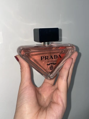 Prada Paradoxe Eau de Parfum 90ml - Prada Paradoxe Eau de Parfum i en unik trekantig glasflaska med ljusrosa doftvätska och svart fyrkantigt lock. Medföljer en snygg rosa kartong med svart detalj. Flaskan rymmer 90 ml och har en modern, elegant design som sticker ut i parfymhyllan.