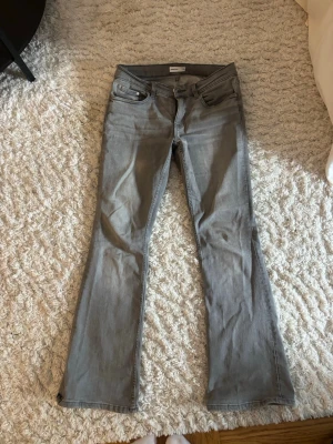 Lågmidjade bootcut jeans - Säljer ett par grå bootcut jeans och klassisk femficksdesign. Jeansen har bälteshällor, knappgylf och är tillverkade i ett mjukt denimtyg. Perfekta till en avslappnad stil och passar till det mesta i garderoben.