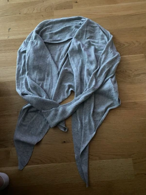 Ljusgrå lång kofta med knytband - Säljer en ljusgrå, tunn och mjuk kofta med långa ärmar och långa knytband framtill. Perfekt att slänga över en topp för en chill och avslappnad look. Materialet känns stretchigt och följsamt.