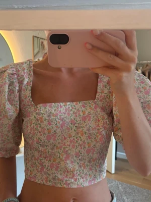 Blommig croppad blus    - Superfin croppad blus med blommigt mönster i rosa, grönt och vitt. Toppen har fyrkantig urringning och puffiga korta ärmar 
