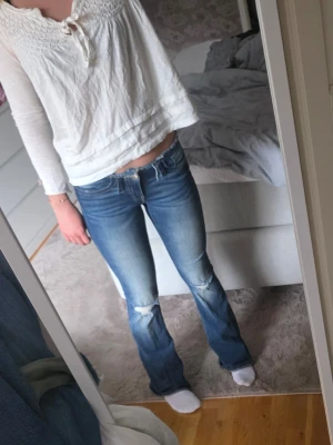 Blå bootcut jeans med slitningar - Säljer ett par blå bootcut jeans med snygga slitningar vid knäna och lätt tvättade detaljer. Jeansen har klassisk femficksdesign och normal midja. Perfekta för en avslappnad och trendig look.