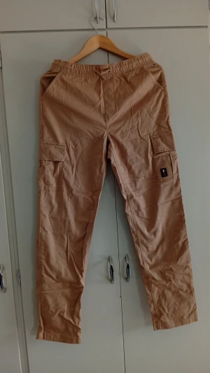Beiga cargobyxor - Säljer ett par beiga cargobyxor från Tommy Hilfiger. Köpta från kidsbrandstore dom är endast testade och säljer pågrund av att de är för små 