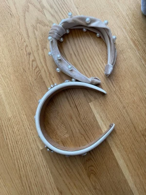 Två diadem med pärlor och dekorationer - Säljer två snygga diadem, ett i beige sammet med pärlor och knutdetalj, och ett i vitt med bred form och stora pärl- och strassdekorationer. Perfekta för att ge en lyxig touch till din look. Båda är vadderade och har en trendig design.