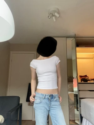 Vit croppad topp med kort ärm - Snygg vit croppad topp med korta ärmar och rund/båt halsringning. Perfekt till jeans eller kjol för en enkel och clean look. Tunn och stretchig, passar dig som gillar minimalistisk stil.