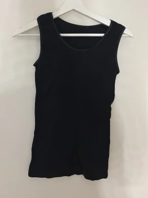Svart ärmlös linnetopp - En enkel och stilren svart linnetopp med rund halsringning och ärmlös design. Perfekt att matcha med jeans eller kjol för en clean look. Materialet känns mjukt och följsamt mot kroppen skulle säga att den är i storlek S, dock är den väldigt elastisk.