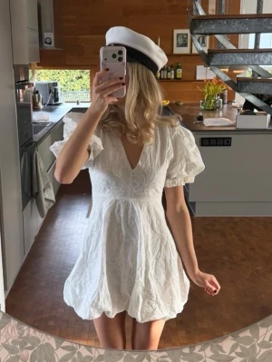 Vit kort klänning med puffärmar - Superfin vit kort klänning med v-ringning och puffiga korta ärmar. Klänningen har ett subtilt broderat blommönster och en lätt volang nedtill. Perfekt för student eller sommarens alla tillfällen! Det är storlek M men det är INTE korrekt. Min vän på bilden är 167 cm lång och oftast xxs. Oanvänd med prislapp. 