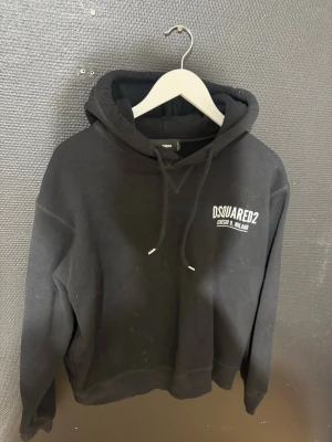 Svart hoodie från Dsquared2 - Cool svart hoodie från Dsquared2 med vit logotyp på bröstet och texten 'Ceresio 9, Milano'. Klassisk passform med huva och dragsnören. Perfekt för dig som vill ha en stilren och trendig look. Materialet känns mjukt och bekvämt.