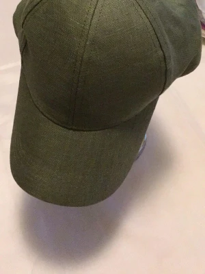 Olivgrön keps i linne - Snygg olivgrön keps med klassisk böjd skärm och sex paneler. Tillverkad i linne för en luftig och avslappnad känsla. Justerbar baktill för perfekt passform. Perfekt accessoar för en casual och trendig stil.